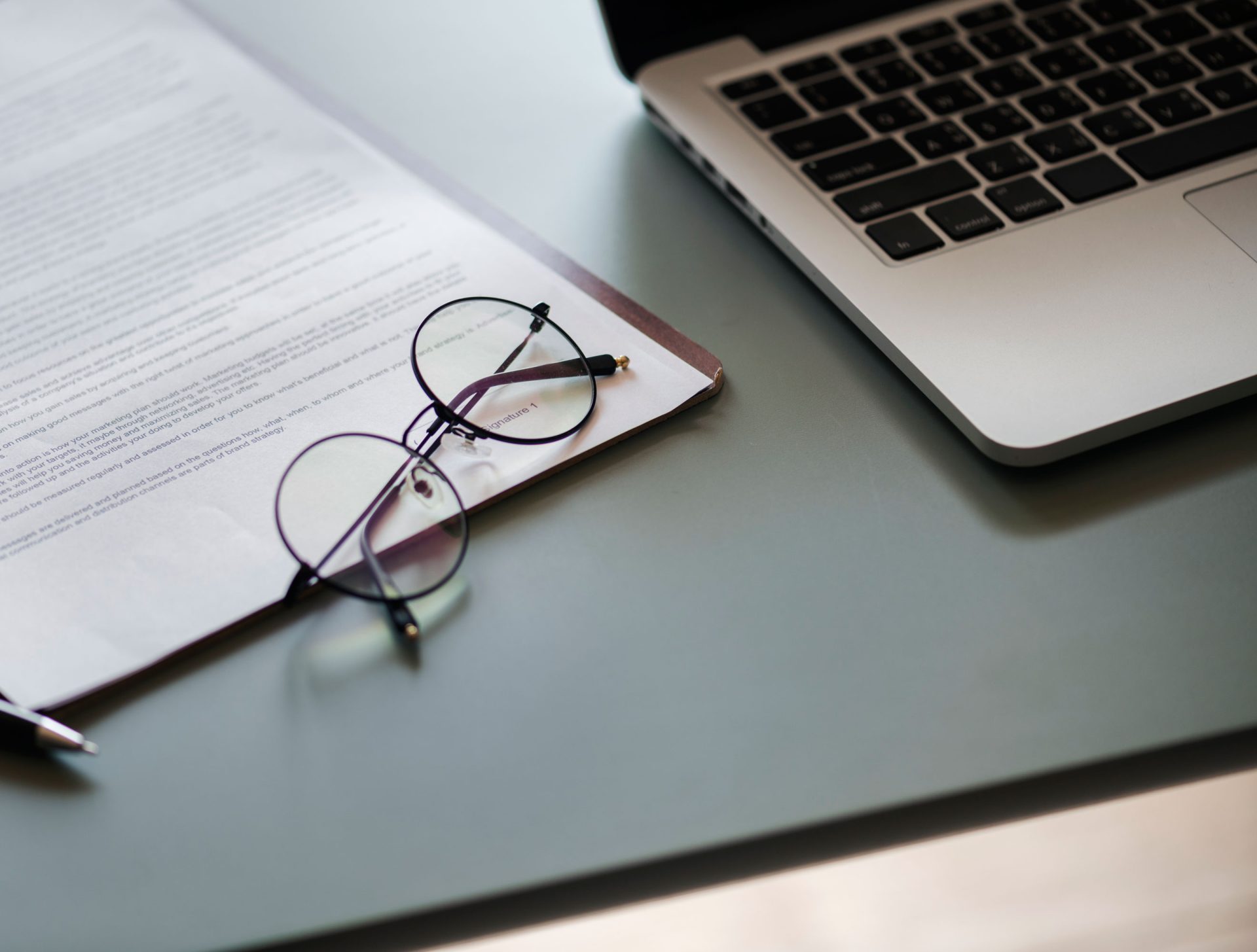 Gafas sobre un documento con un portátil al lado